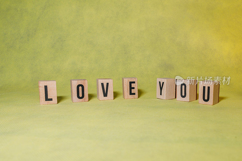单词LOVE YOU由黄色背景上的木制字母构成，并带有复制空间，以传达信息广告概念